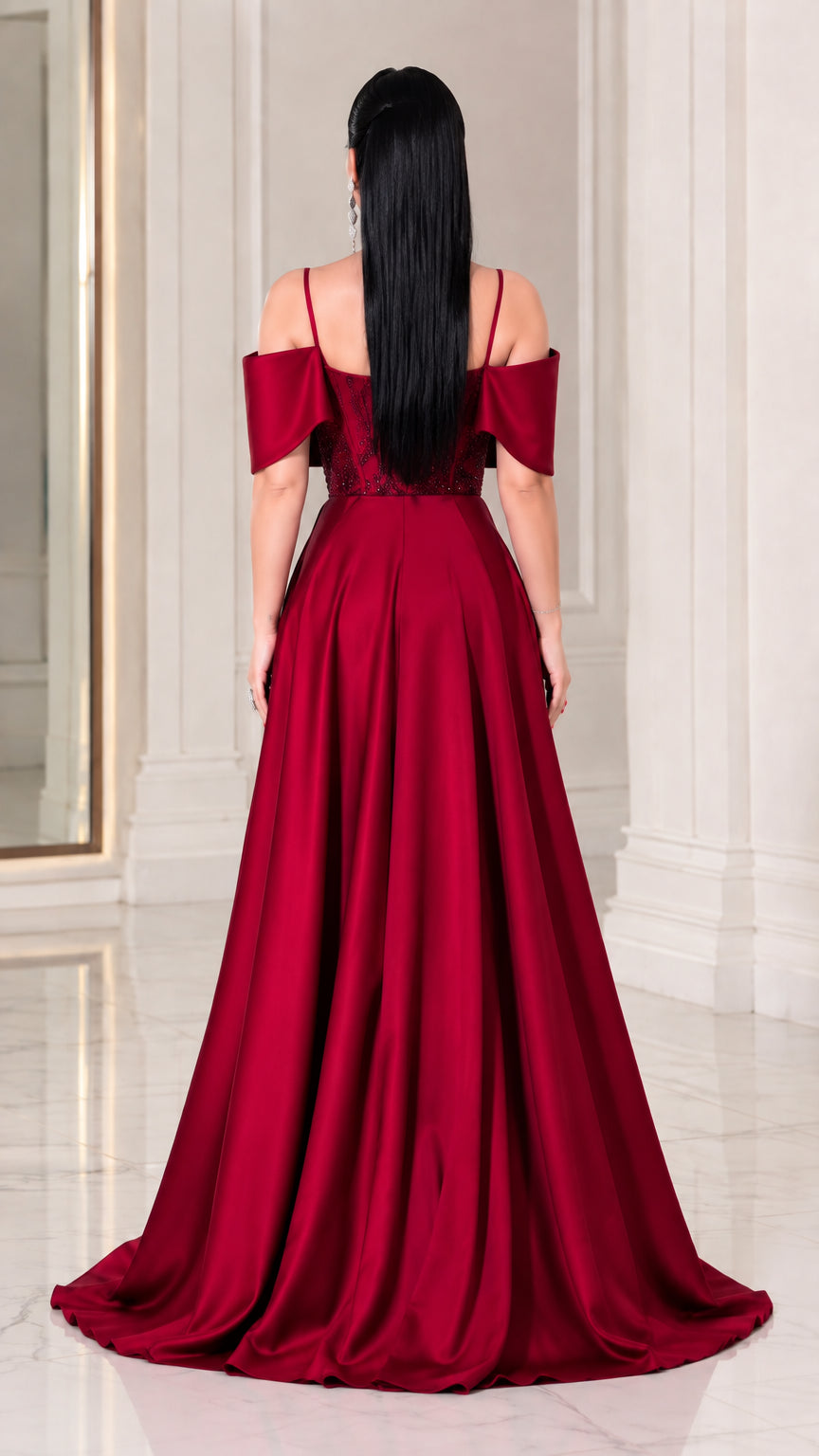 Back view of model showing the flowing satin-finish overskirt and cold-shoulder back design in Wine Red