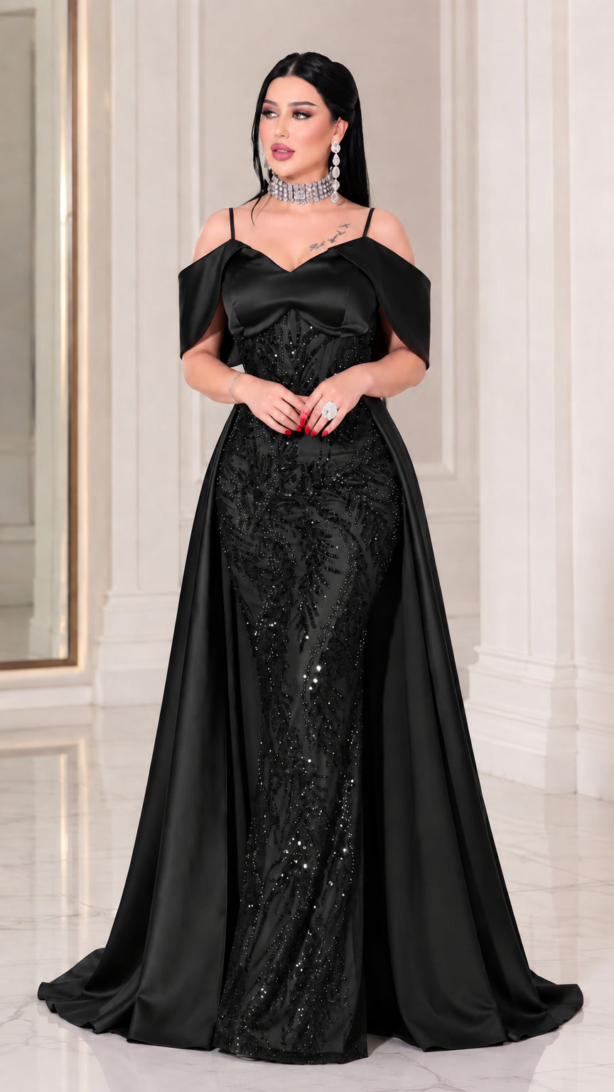 Full-length front view of model wearing Black beaded off-the-shoulder mermaid gown with overskirt