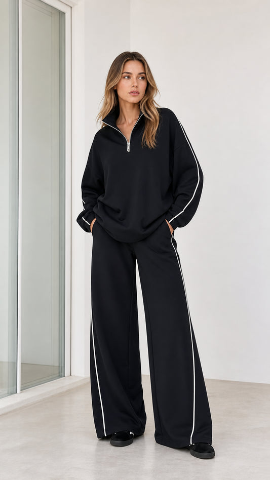 Front full-body view of model wearing black half zip sweatshirt and wide leg pants 2-piece set with white piping